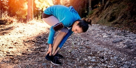 Vrouw die haar enkel controleert tijdens het hardlopen
